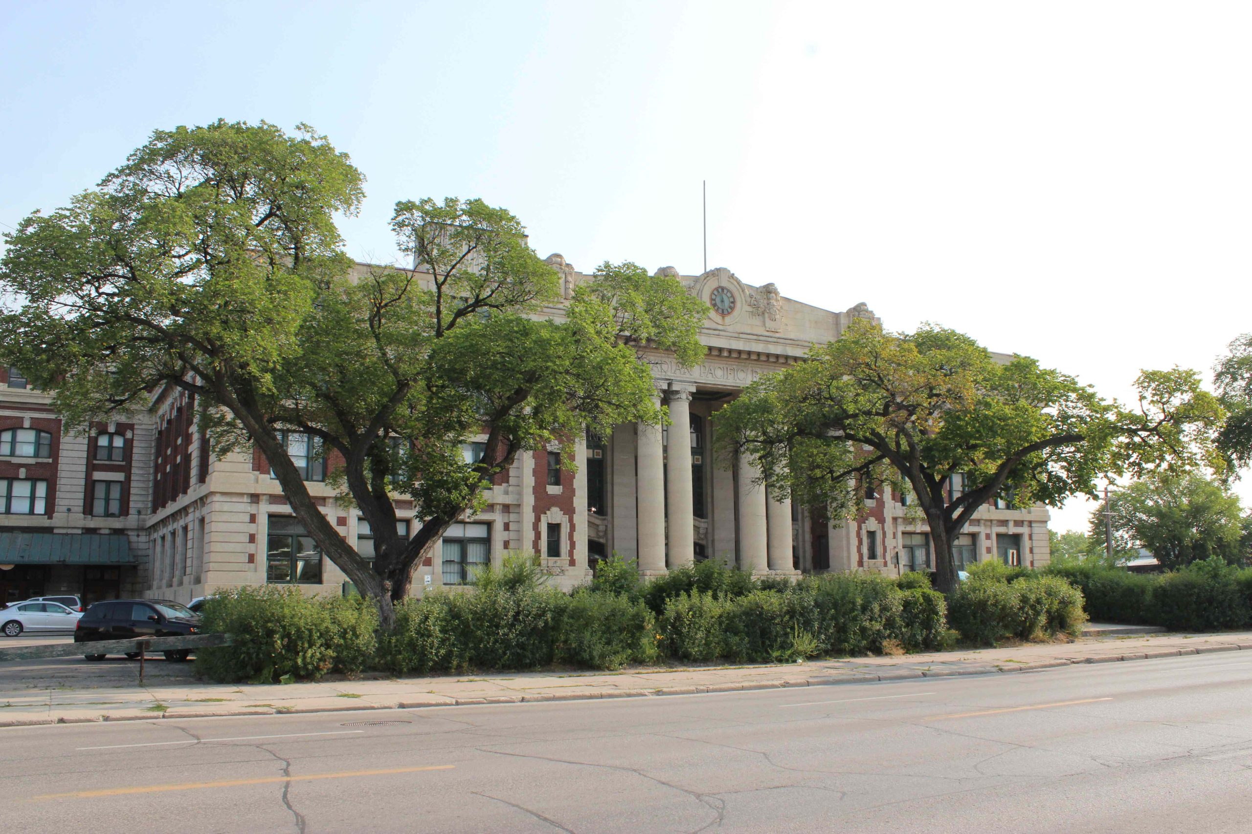 A picture of 181 Higgins Pillar Doors on an angle facing the east from across Higgins. includes greenery and the sky.