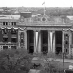 a black and white aerial photo of 181 Higgins pillar doors, 19th century, The pillars have banners over them, and the building is decorated.
